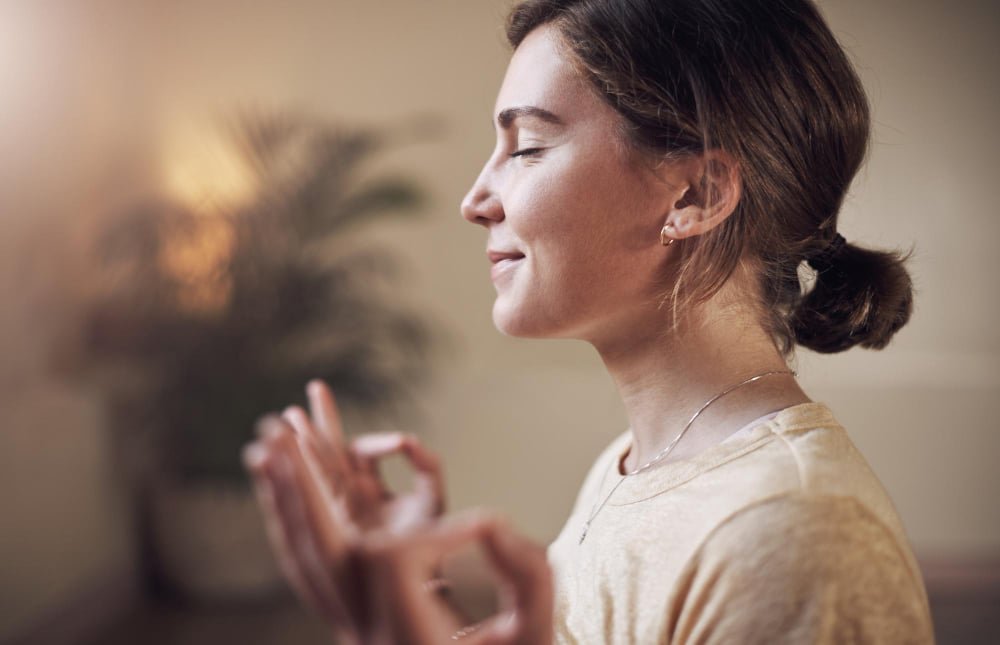 Mujer joven con los ojos cerrados practicando respiración consciente en un entorno tranquilo.